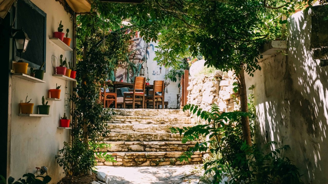 Yeşilliklerle çevrili taş basamaklar ve renkli saksılarla süslenmiş Ege köyünde bir sokak